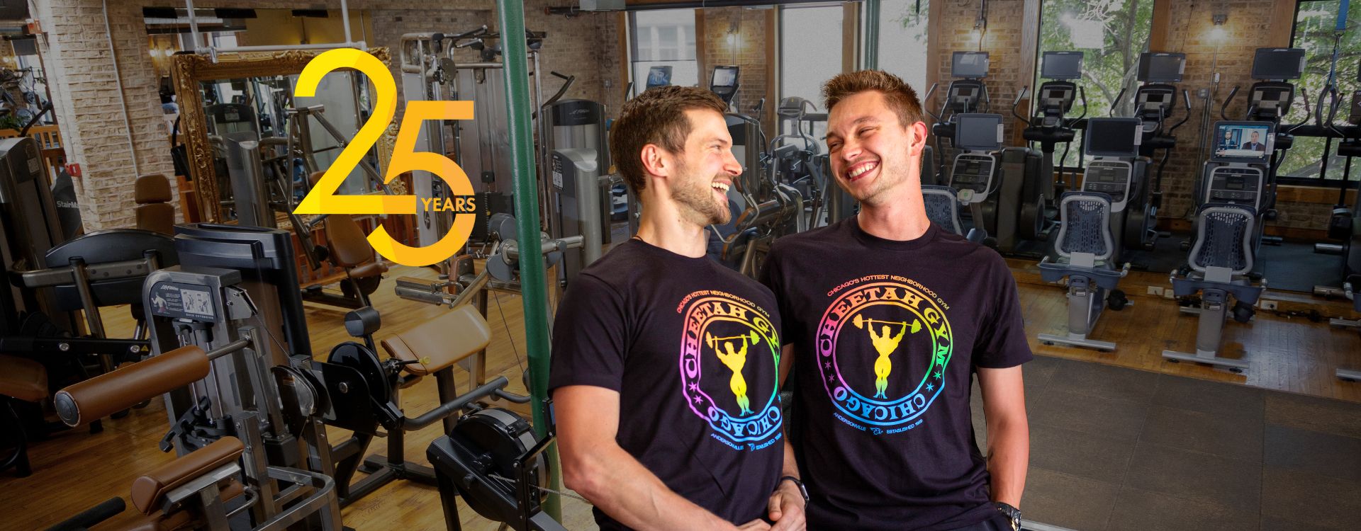 Two men wearing Pride-themed Cheetah Gym apparel standing in front of gym equipment with a banner reading ‘Everyone is welcome’ — promoting inclusivity and LGBTQ+ support at Chicago’s Cheetah Gym.